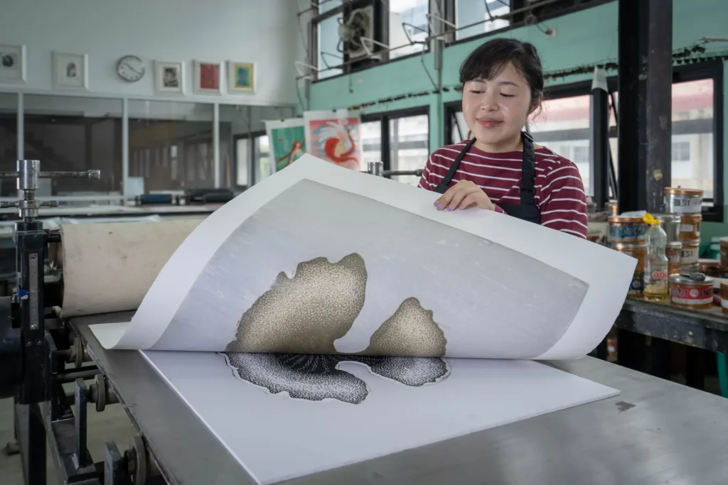Printmaker lifting a fresh print from the press